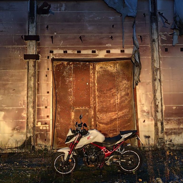 Honda CB750 Hornet Weiße Motorrad vor einer alten, verfallenen Mauer mit rostigen Türen.