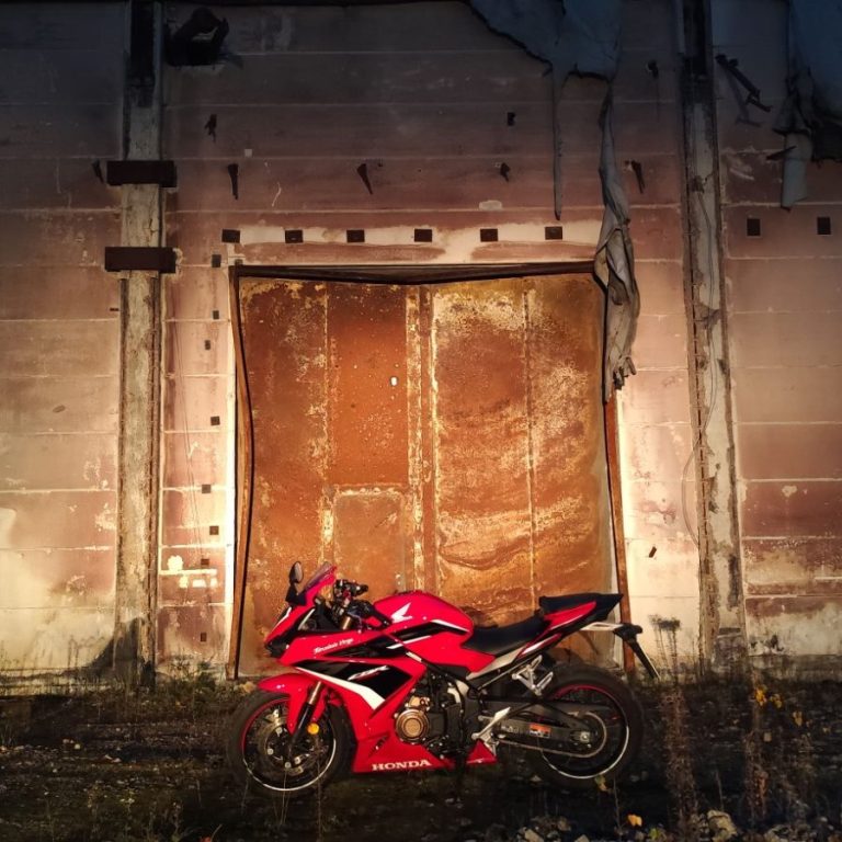Honda CBR500R Rotes Motorrad vor einer alten, rauen Wand mit einer rostigen Tür.