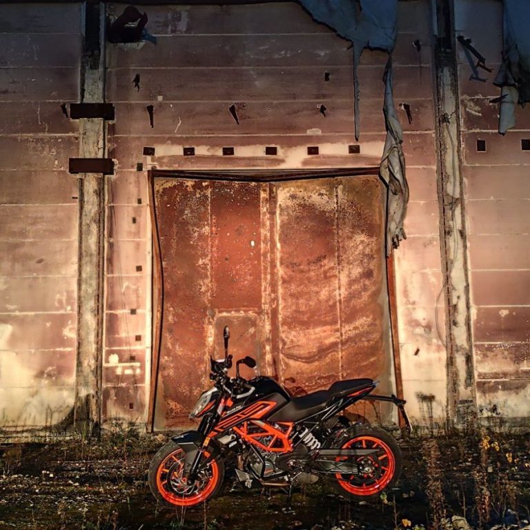 KTM 125DUKE Schwarzes Motorrad mit orangefarbenen Akzenten vor einer alten, rostigen Wand.
